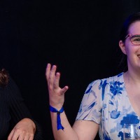 Girl smiling as she talks into microphone and the girl next to her smiles while she talks